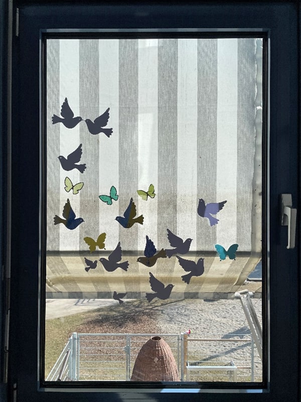 11 verschieden farbige Papier-Friedenstauben und 5 Schmetterlinge verzieren eine Fensterscheibe.